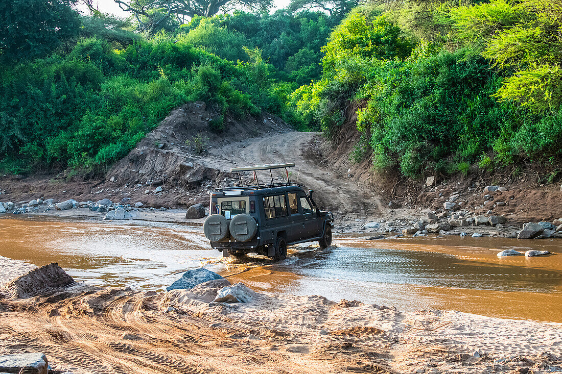 Safari-Fahrzeug durchquert einen seichten Fluss im Lake Manyara National Park, Tansania