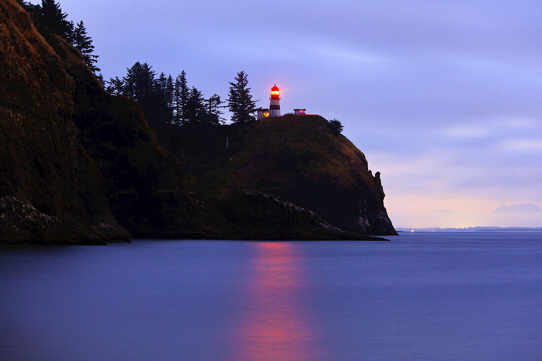 Beleuchteter Leuchtturm an der Küste von Washington in der Abenddämmerung, Cape Disappointment State Park, Washington, Vereinigte Staaten von Amerika