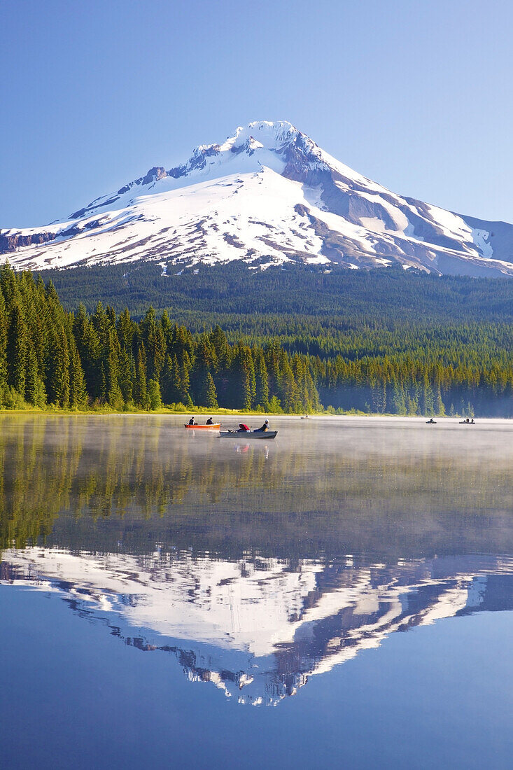 Mirror image of Mount Hood and forest reflected in Trillium Lake with mist rising off the water and people boating and fishing in the tranquil water,Oregon,United States of America