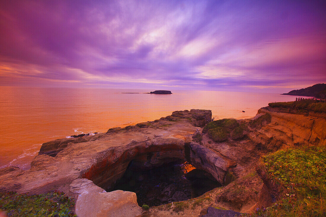 Warm sunset light over the Oregon coast with tranquil water and rugged cliffs and the horizon in the distance,Oregon,United States of America