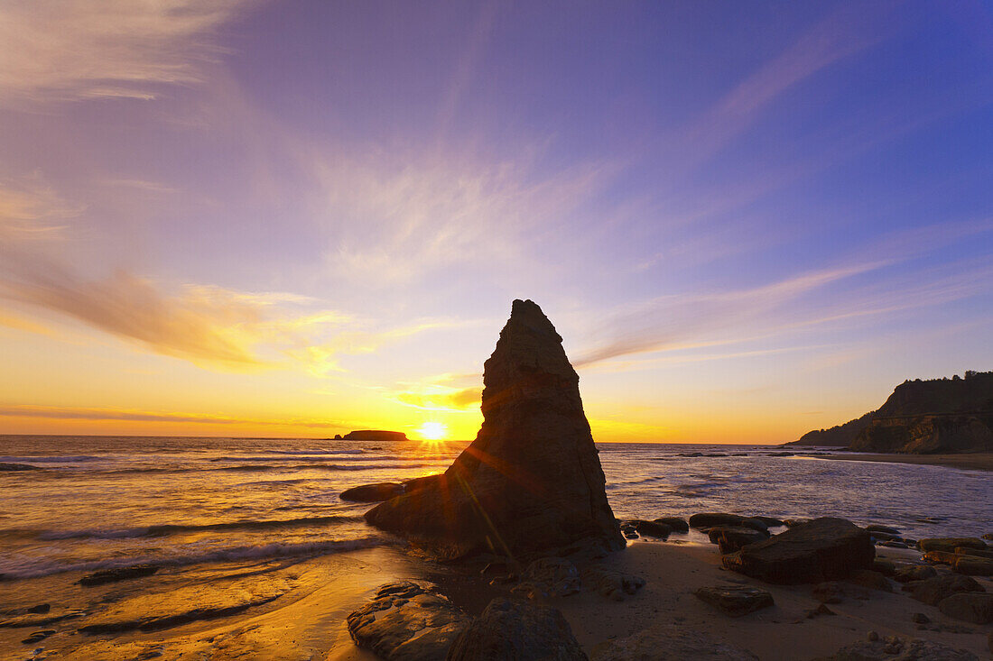 Goldener Sonnenaufgang über dem Horizont des Pazifischen Ozeans an der Küste von Oregon mit ruhigem Wasser und silhouettierten Felsformationen, Oregon, Vereinigte Staaten von Amerika