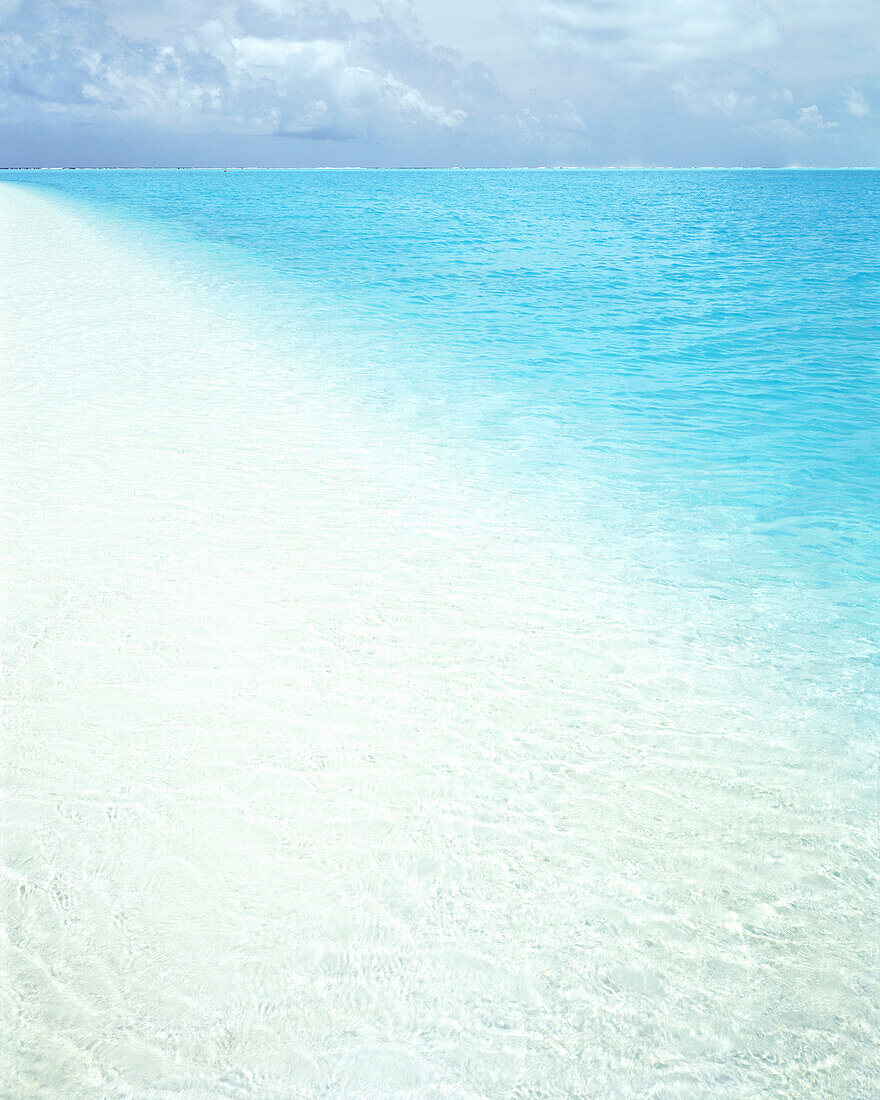 Turquoise ocean water stretching to the horizon and white sand along a tropical island,Cook Islands