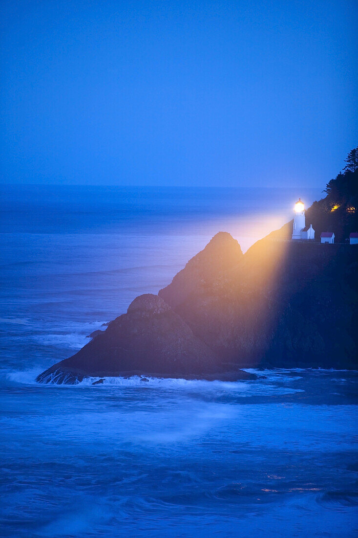 Leuchtturmlampe, die in der Morgendämmerung die Küstenlinie durch den Nebel beleuchtet,Oregon-Küste,Oregon,Vereinigte Staaten von Amerika