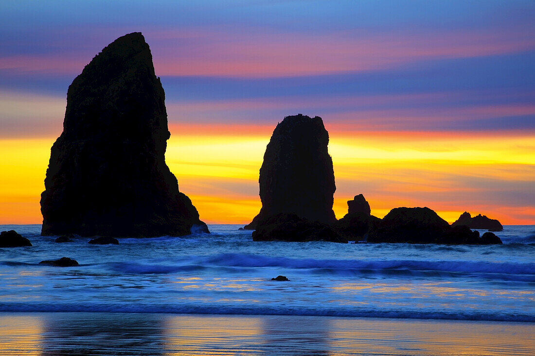 Silhouettierte Meeresstapel entlang der Küste von Oregon bei Sonnenuntergang, wobei der Himmel in verschiedenen Farben leuchtet, Ecola State Park, Cannon Beach, Oregon, Vereinigte Staaten von Amerika