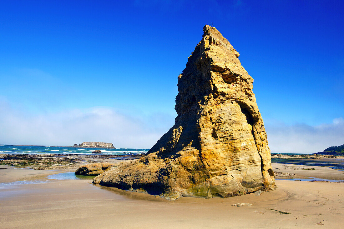 Zerklüftete Felsformation mit Spitze an einem Strand entlang der Küste von Oregon mit Blick auf den Horizont über dem Pazifik, Oregon, Vereinigte Staaten von Amerika
