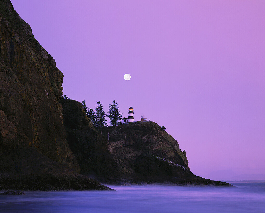 Cape Disappointment Lighthouse auf einer Landzunge in der Abenddämmerung an der Küste Washingtons mit violett leuchtendem Himmel und Vollmond,Washington,Vereinigte Staaten von Amerika