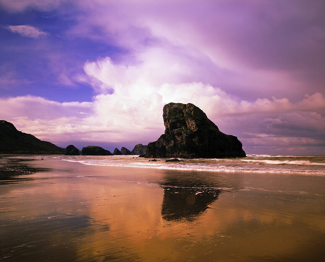 A rock formation is reflected in the wet sand on a beach in Cape Sebastian along the Oregon coast with dramatic cloud formations over the ocean,Oregon,United States of America