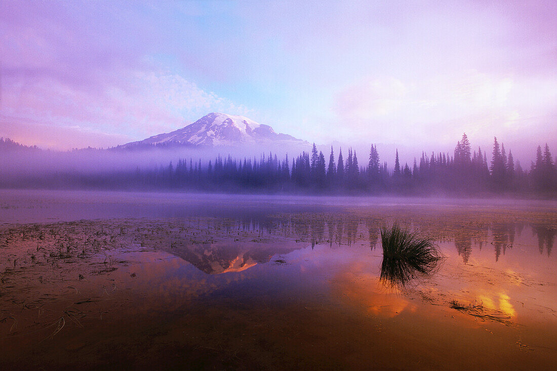 Mount Rainier bei Sonnenaufgang mit Nebel und warmen Farben, die sich im See spiegeln, Mount Rainier National Park, Washington, Vereinigte Staaten von Amerika