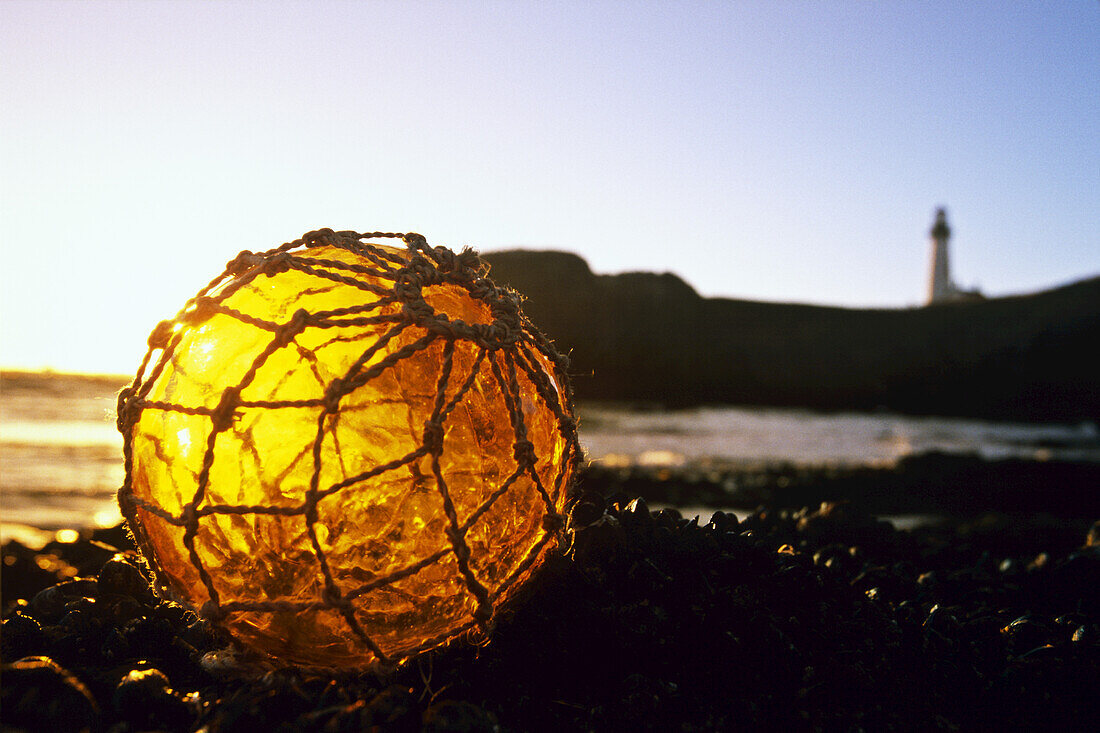 Fischerboot im Gegenlicht des Sonnenuntergangs an der Küste von Oregon mit dem Yaquina Head Light im Hintergrund, Yaquina Bay State Park, Oregon, Vereinigte Staaten von Amerika