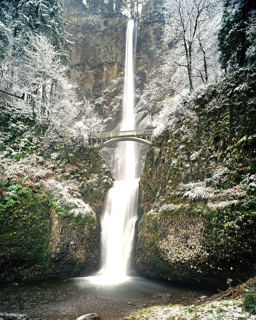 Footbridge over Multnomah Falls in winter with frosty foliage along the high rock cliffs,Oregon,United States of America