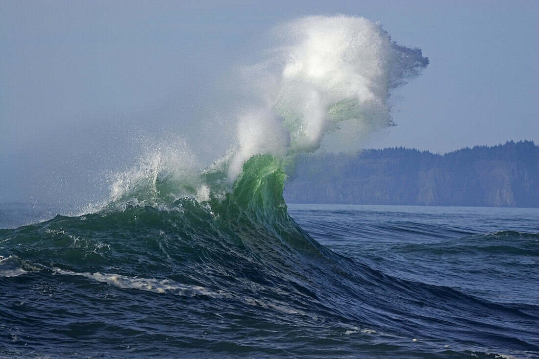 Dramatic splashing wave reaching high with spray as it breaks at the shore with the Oregon coastline in the background at Cape Kiwanda,Pacific City,Oregon,United States of America