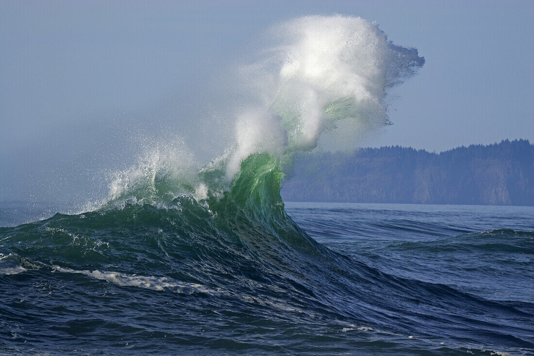 Dramatische, hoch aufspritzende Welle, die sich am Ufer bricht, mit der Küstenlinie von Oregon im Hintergrund am Cape Kiwanda, Pacific City, Oregon, Vereinigte Staaten von Amerika