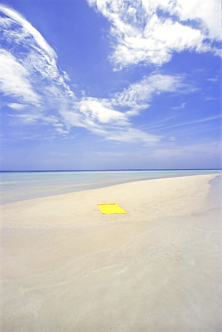 Ein leuchtend gelbes Strandtuch liegt auf einem Stück weißen Sand, umgeben von türkisfarbenem Meerwasser auf den Malediven, Malediven, Republik Malediven