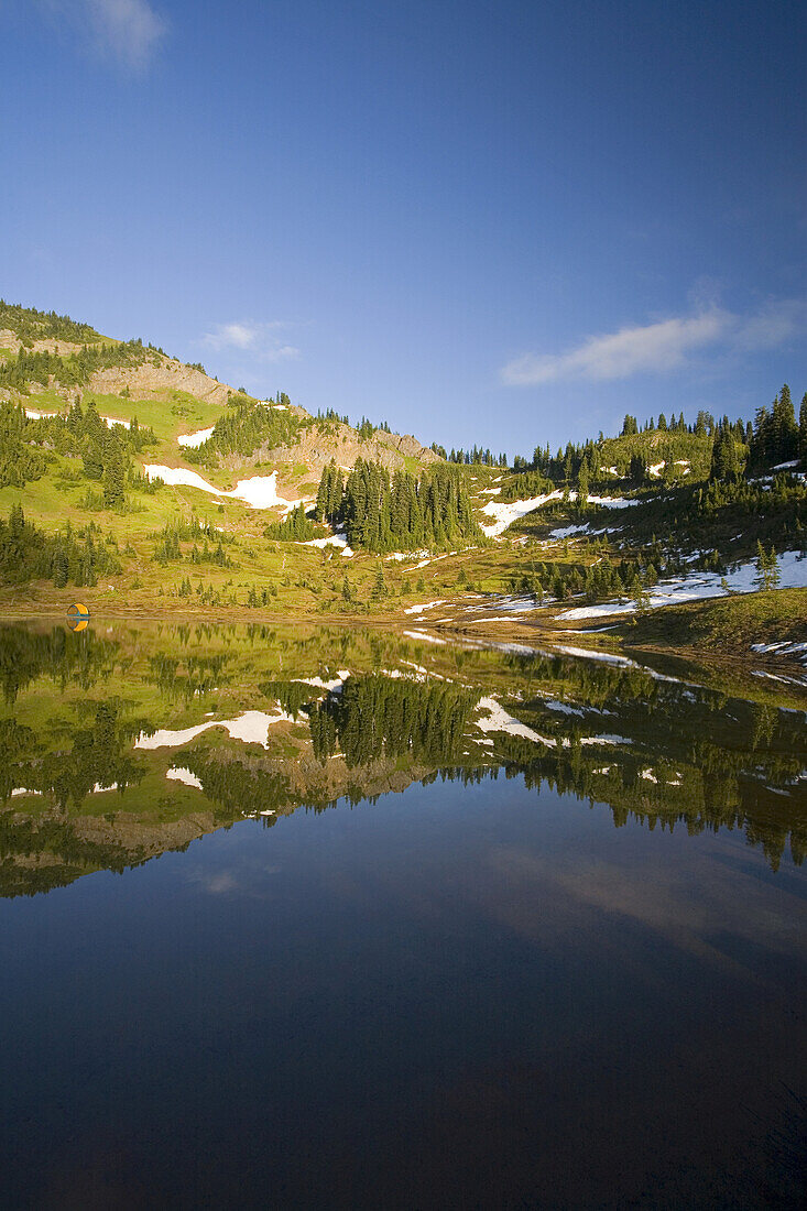 Ein Zelt am Ufer des ruhigen Tipsoo Lake in den Bergen mit Spuren von Schnee an den Hängen und einem Spiegelbild, das sich auf der Oberfläche des Sees spiegelt, Mount Rainier National Park, Washington, Vereinigte Staaten von Amerika