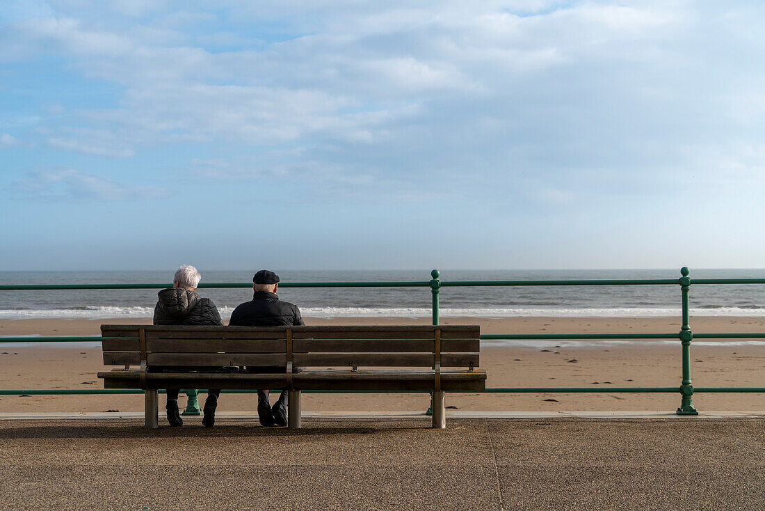 Älteres Ehepaar sitzt auf einer Bank am Wasser und blickt auf den Ozean,Sunderland,Tyne and Wear,England