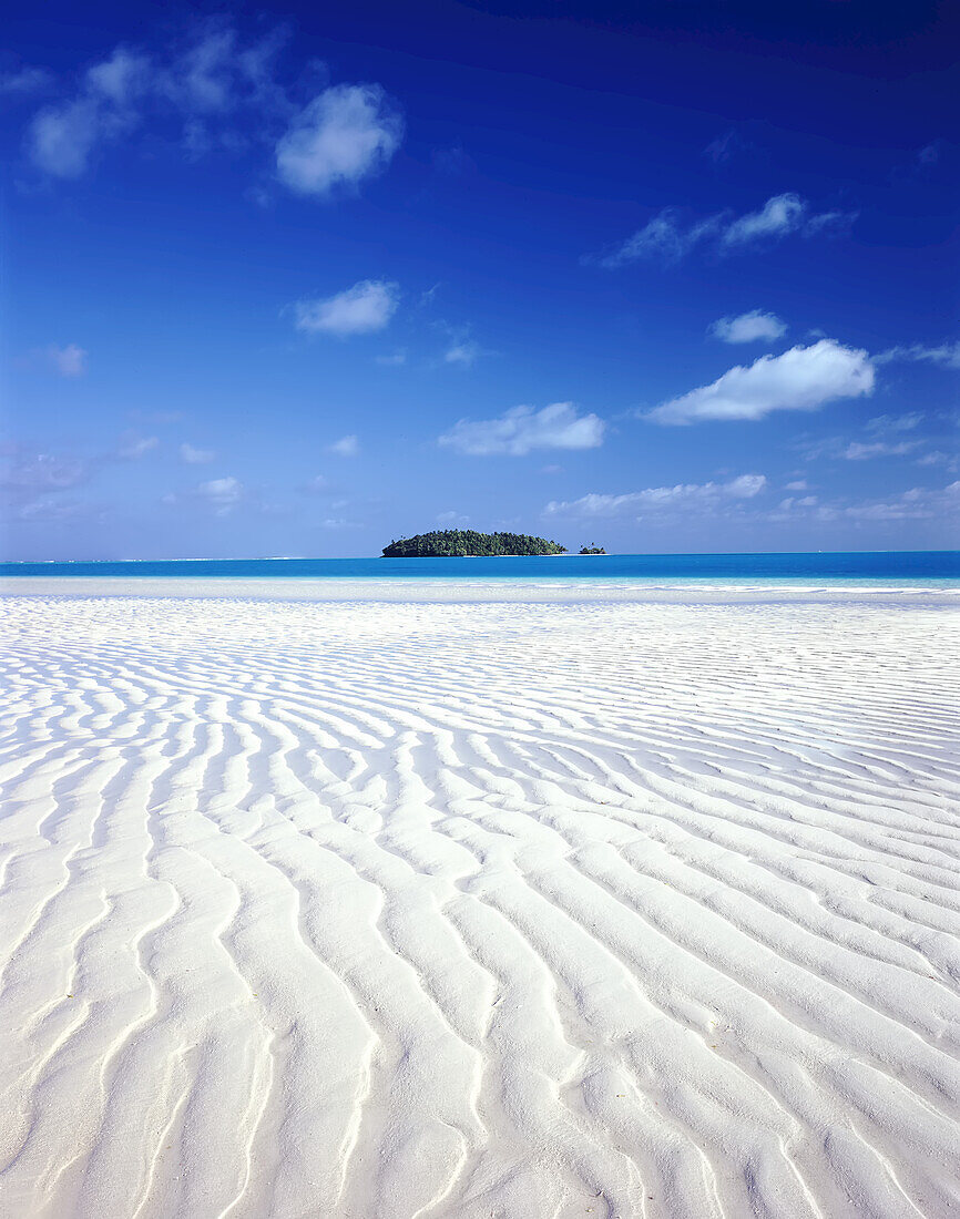 Kleine Insel auf den Cook-Inseln, umgeben von strahlend blauem Ozeanwasser und einem Atoll mit weißem Sand im Vordergrund, Cook-Inseln