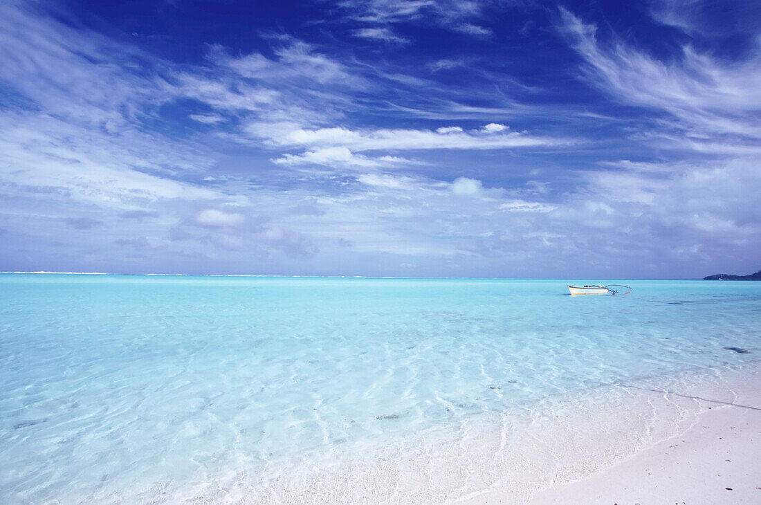 Türkisfarbenes Meerwasser vor einem weißen Sandstrand mit einem kleinen Ruderboot, das vor dem Ufer in Bora Bora, Französisch-Polynesien, vertäut ist