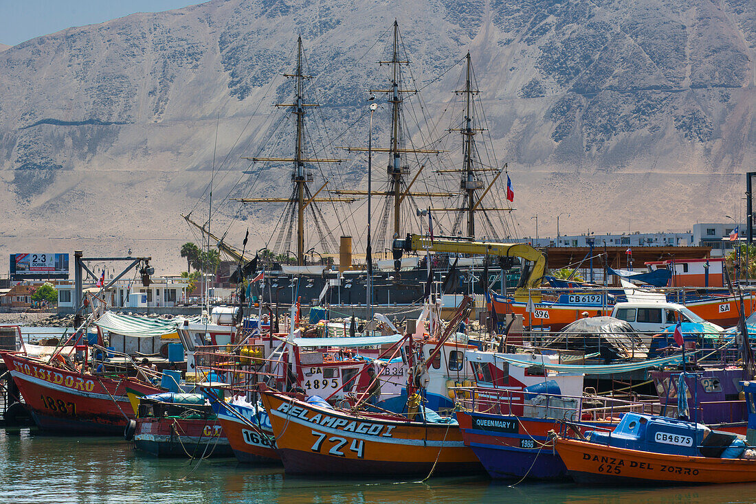 Fischerboote und die Masten eines Großseglers im Hafen von Iquique vor einem Wüstenhügel,Iquique,Chile