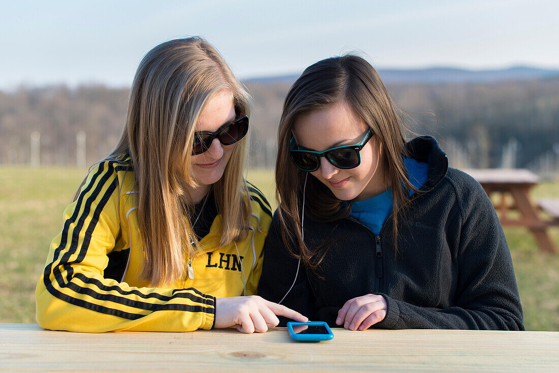 Teenager schauen auf ein Smartphone, während sie die gleichen Kopfhörer benutzen.