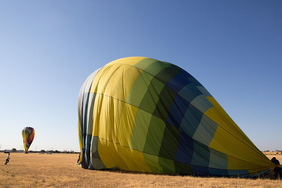 Several people deflate hot air balloons in an open field.,Winters,California