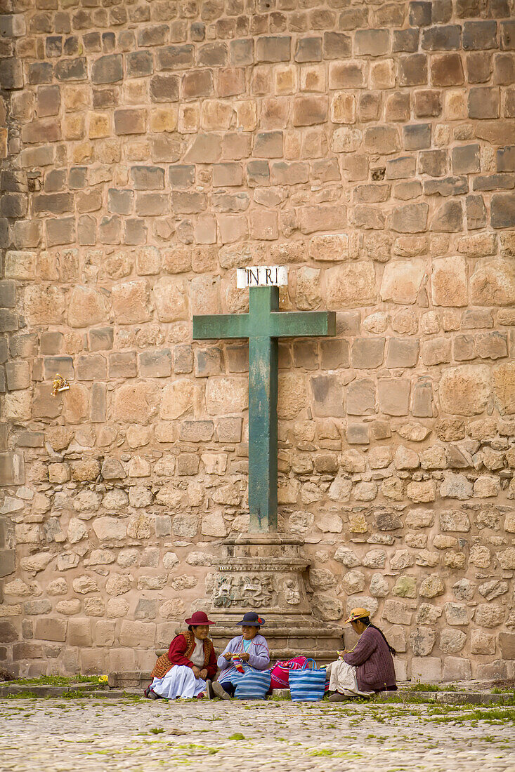 Peruanische Frauen machen Kunsthandwerk am Fuße eines Kreuzes.