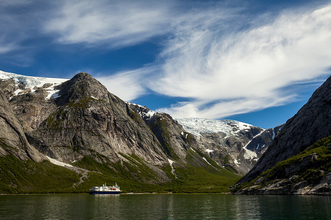 A distant cruise ship amid coastal snow-capped mountains.