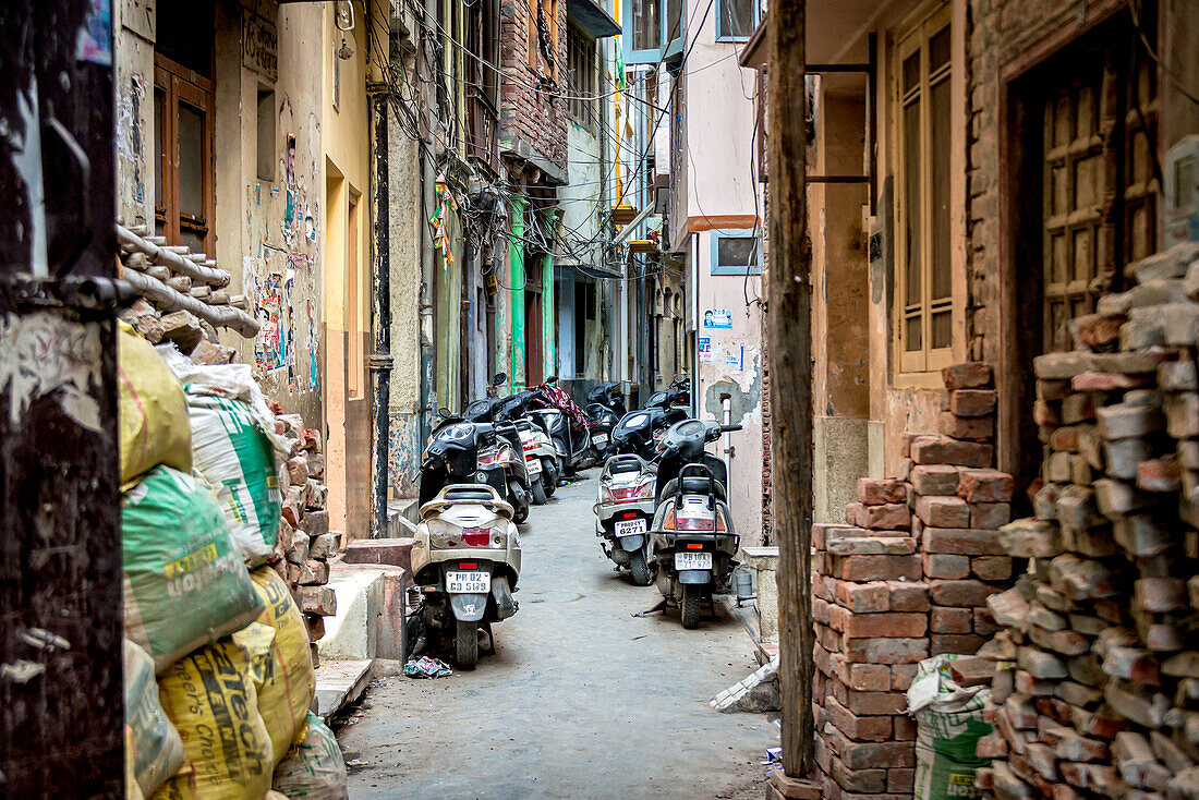 Geparkte Motorräder säumen eine enge Gasse in Indien, Amritsar, Punjab, Indien