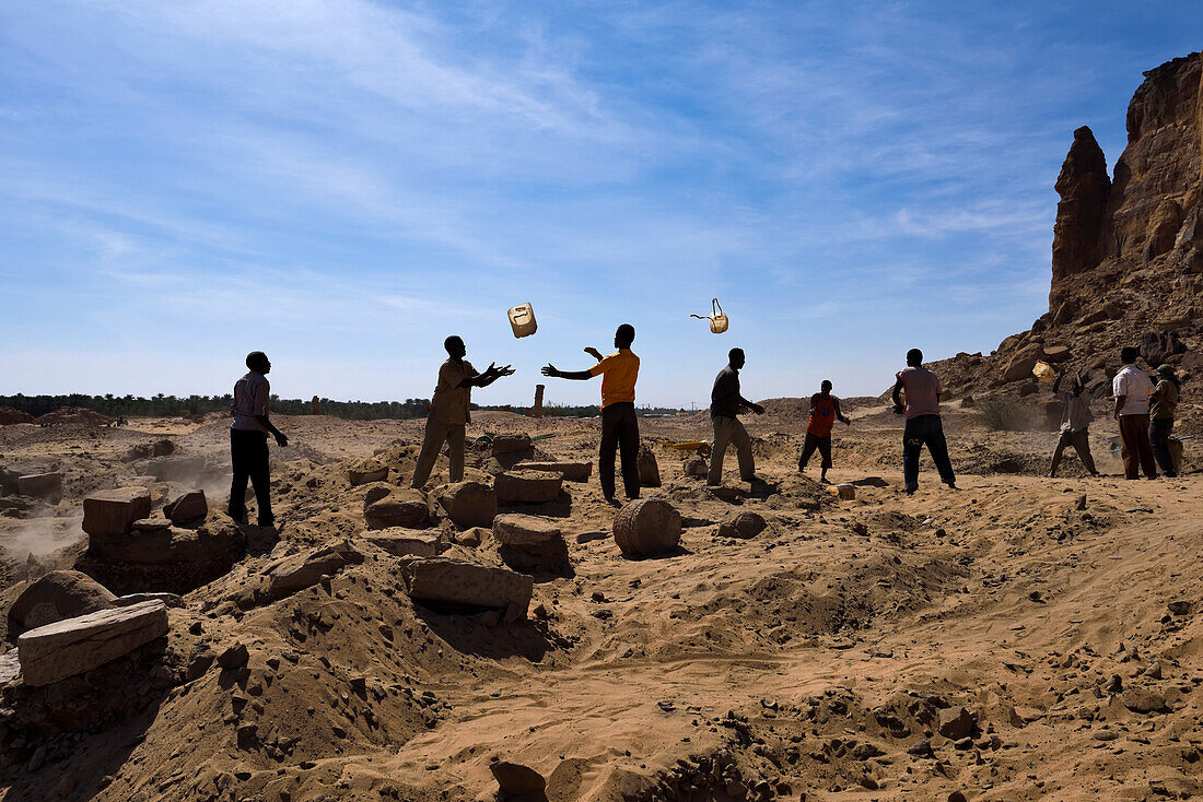 Sudanesische Arbeiter werfen sich gegenseitig Eimer zu, um Sand effizient zu transportieren und archäologische Überreste zu erhalten,Meroe,Sudan,Afrika.