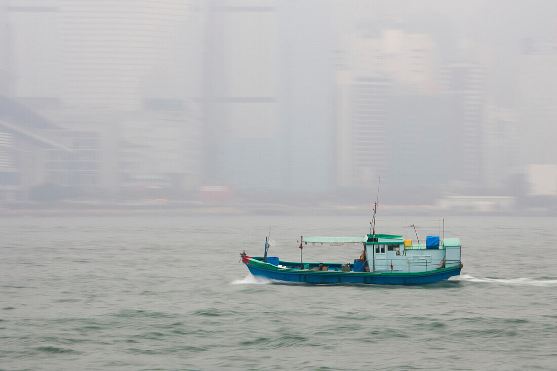 A boat crosses the harbor in front of a foggy Hong Kong.