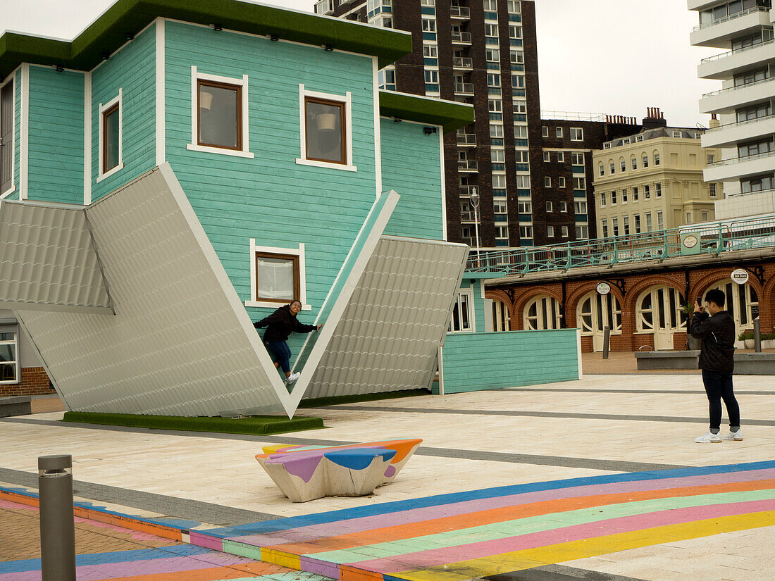 Asiatische junge Frau posiert für ein Foto vor dem Upside Down House, Brighton, East Sussex, England