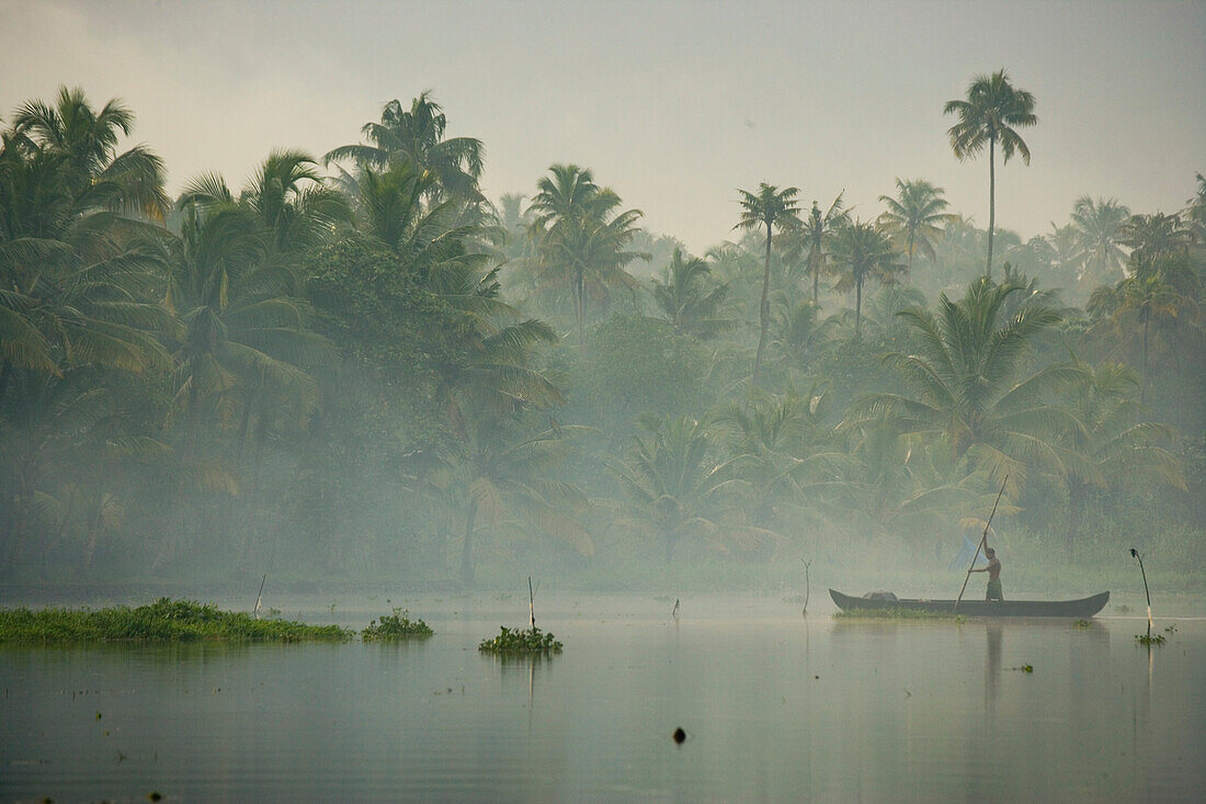 Junger Mann schiebt ein Kanu im Regen flussabwärts, Bundesstaat Kerala, Indien