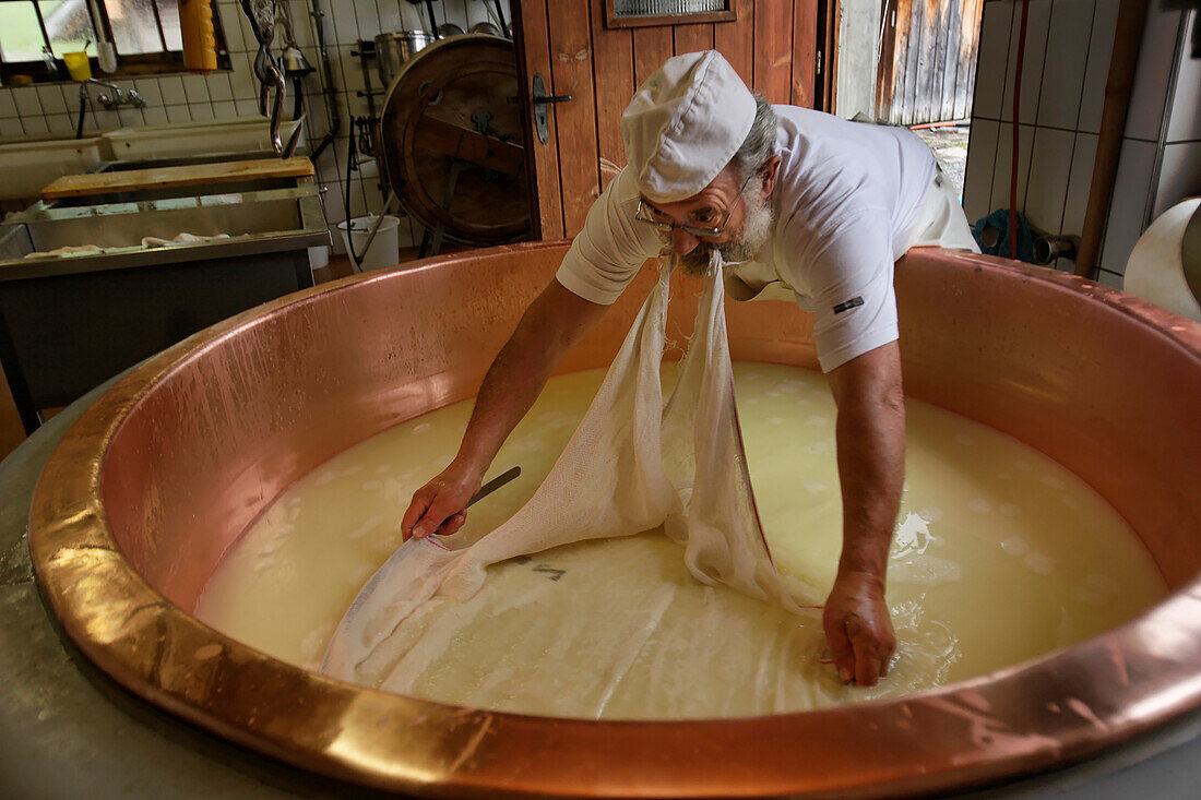 Ein Arbeiter breitet das Käsetuch aus, während er in einem Kupferkessel Alkase-Käse herstellt. Ein charakteristisches Merkmal von Schweizer Käse ist die Verwendung von Kupfer. Um als Gruyère, Emmentaler, Raclette oder sogar französischer Comté bezeichnet zu werden, müssen diese Käse in einem Kupferkessel hergestellt werden, da dieser die Wärme gleichmäßig verteilt,Schweiz