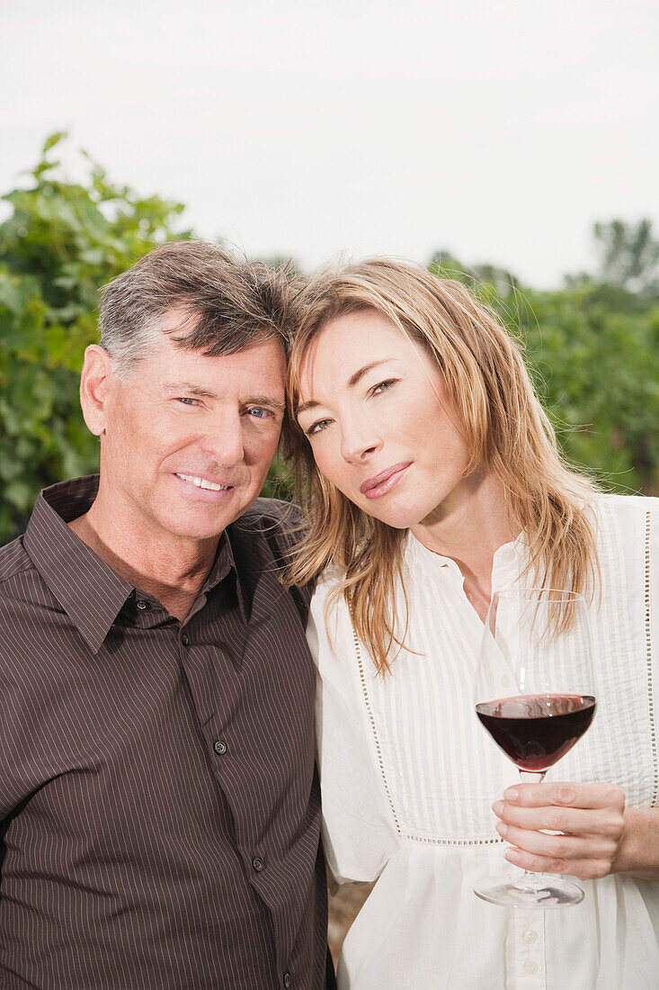 Porträt eines Paares im Weinberg, das ein Glas Wein hält