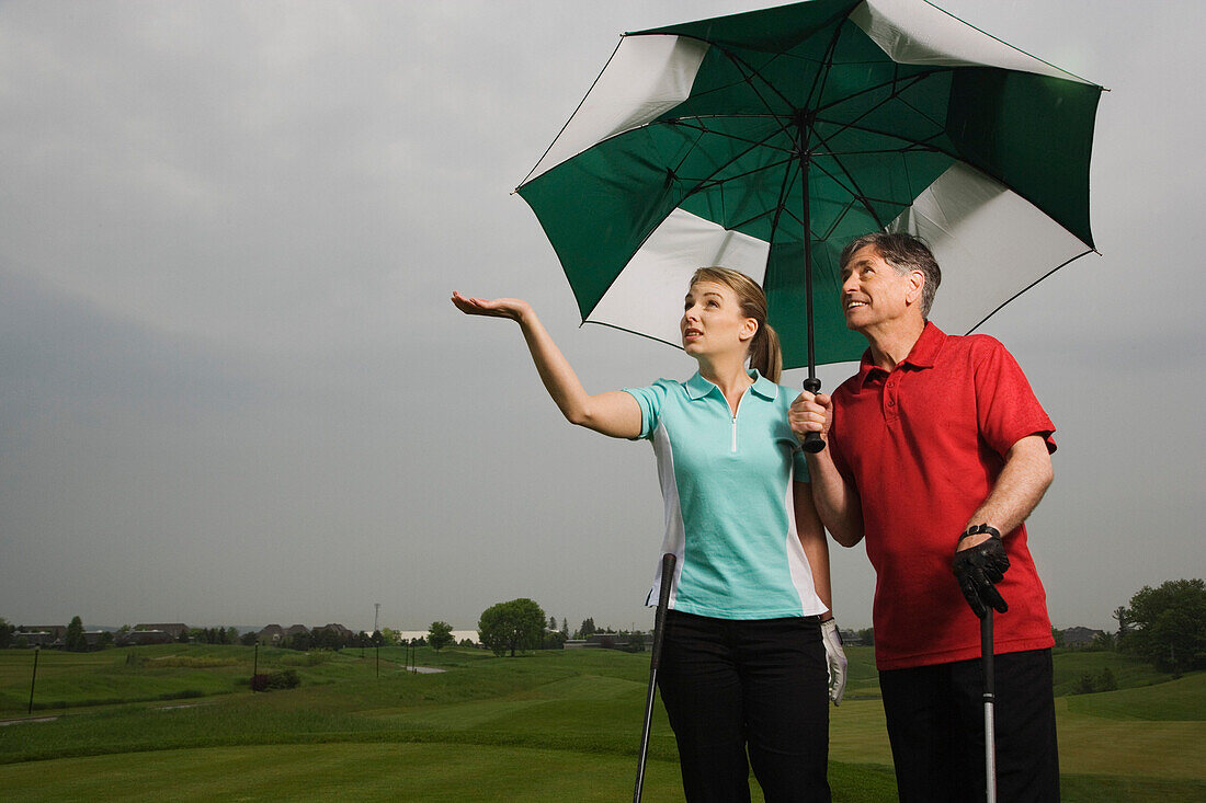 Vater und Tochter auf dem Golfplatz mit einem großen Regenschirm in der Hand