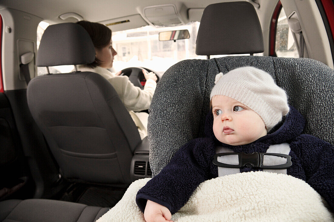 Baby im Autositz mit fahrender Mutter