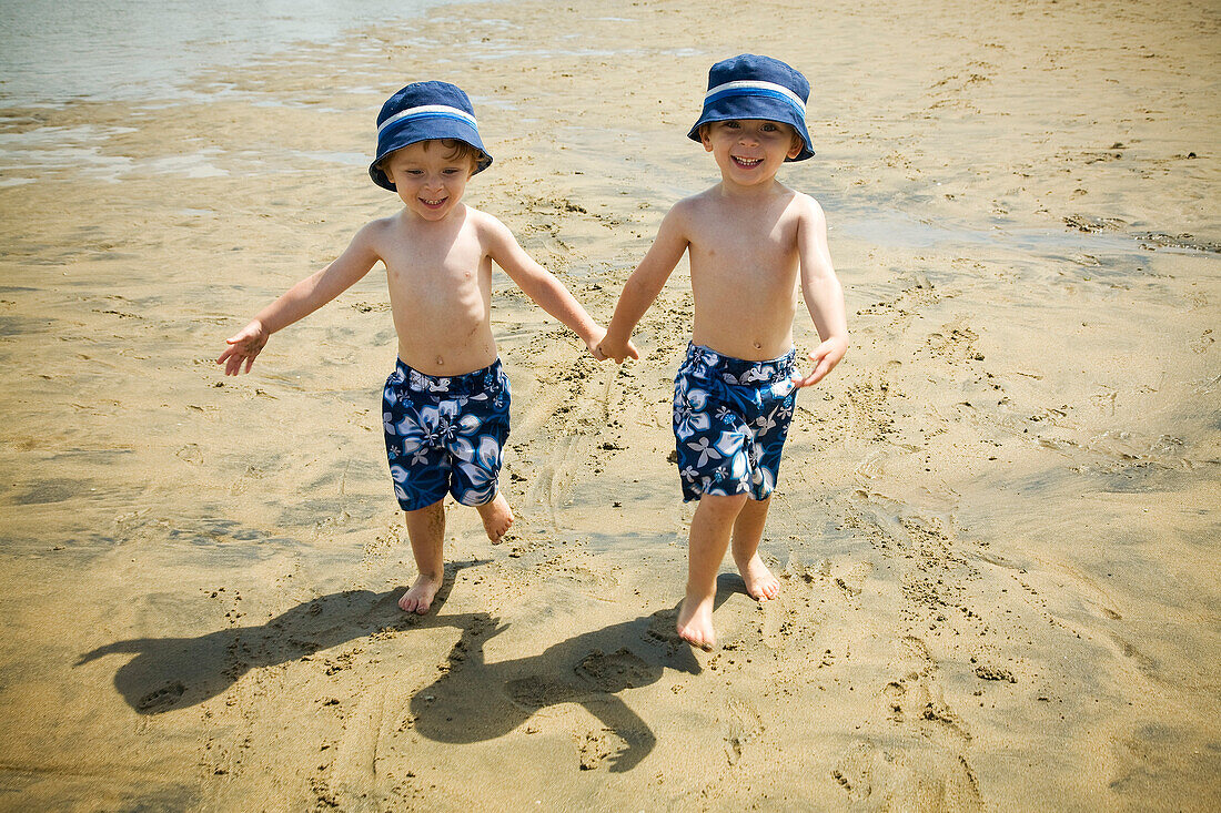 Zwillingsjungen gehen Hand in Hand am Strand spazieren