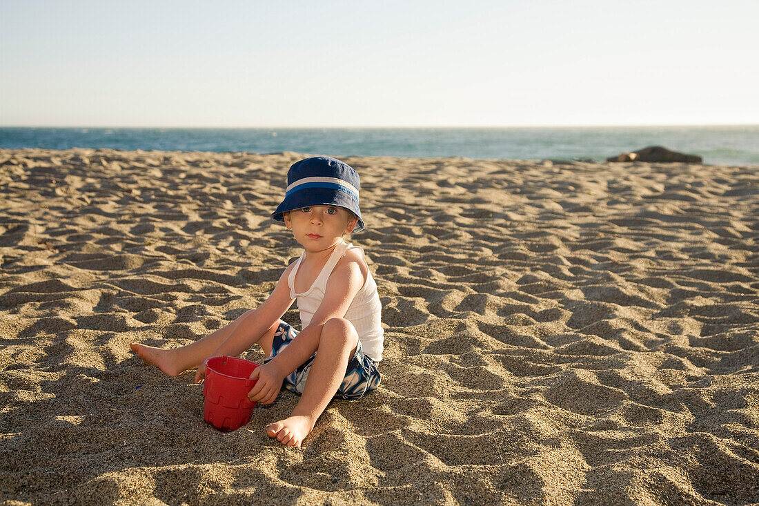 Porträt eines Jungen, der am Strand im Sand gräbt
