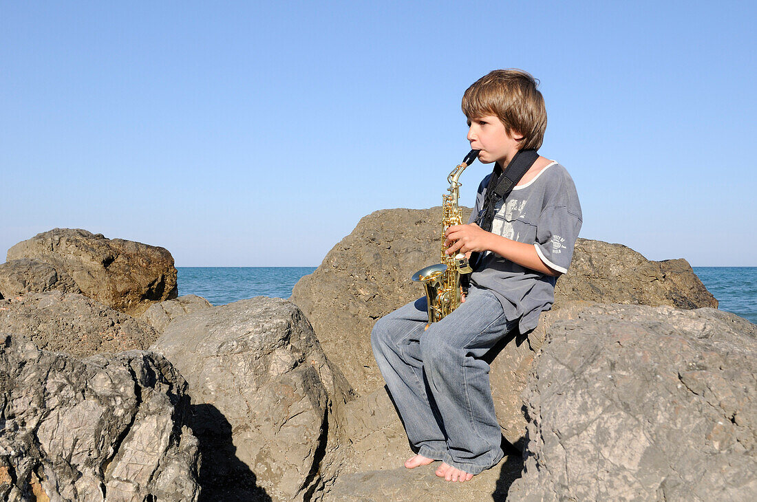Saxophon spielender Junge auf Felsen am Ufer