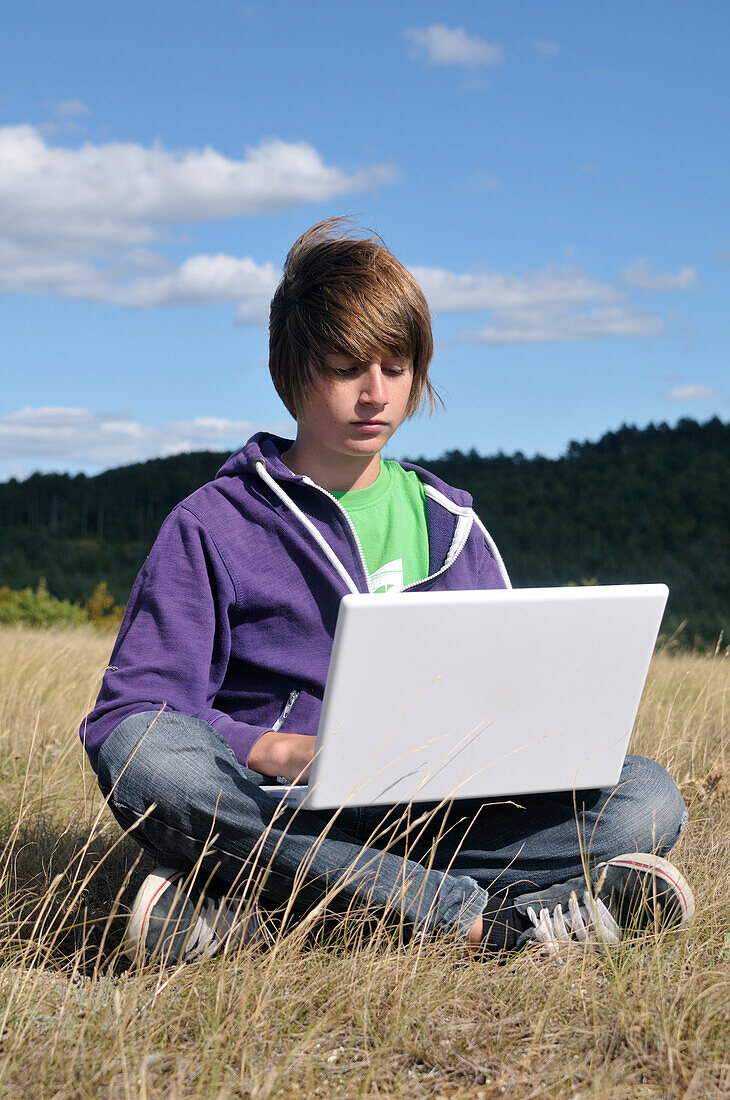 Junge im Feld sitzend mit Laptop-Computer, Blandas, Gard, Frankreich