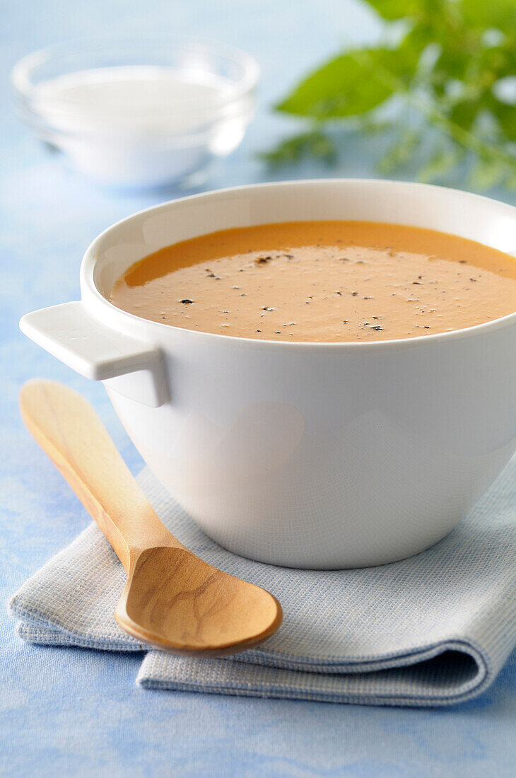 Close-up of Bowl of Pumpkin Soup on Tea Towel with Wooden Spoon on Blue Background,Studio Shot