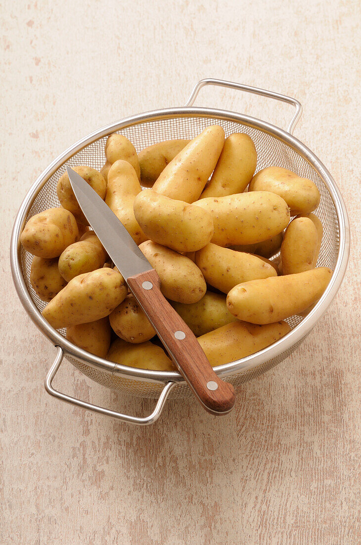 Overhead-Ansicht von Kartoffeln in Sieb mit Messer auf Beige Hintergrund, Studio Shot