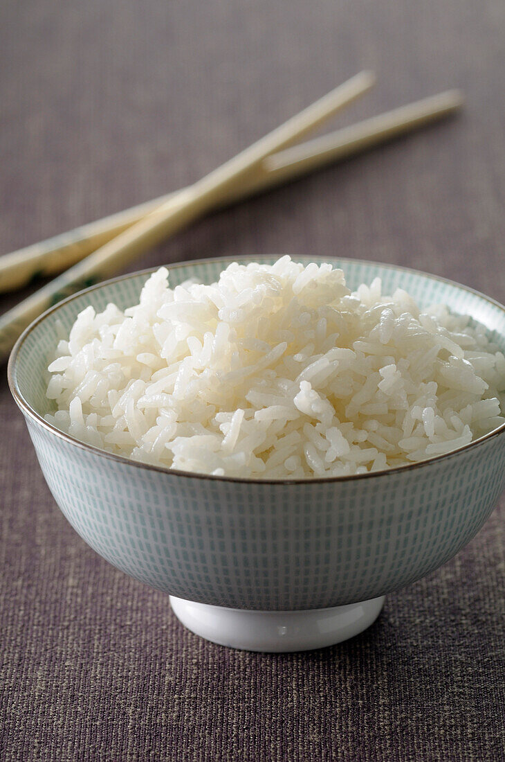 Nahaufnahme einer Schüssel Reis mit Essstäbchen vor grauem Hintergrund,Studioaufnahme