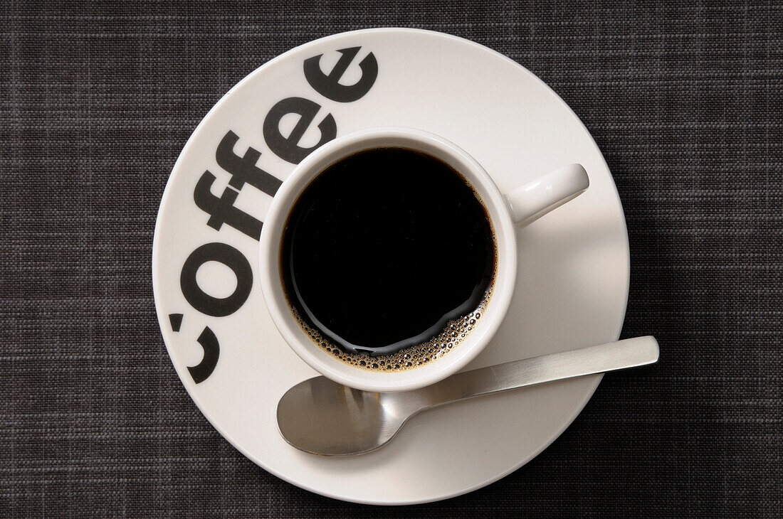 Draufsicht auf eine Tasse mit schwarzem Kaffee auf einer Untertasse mit Löffel