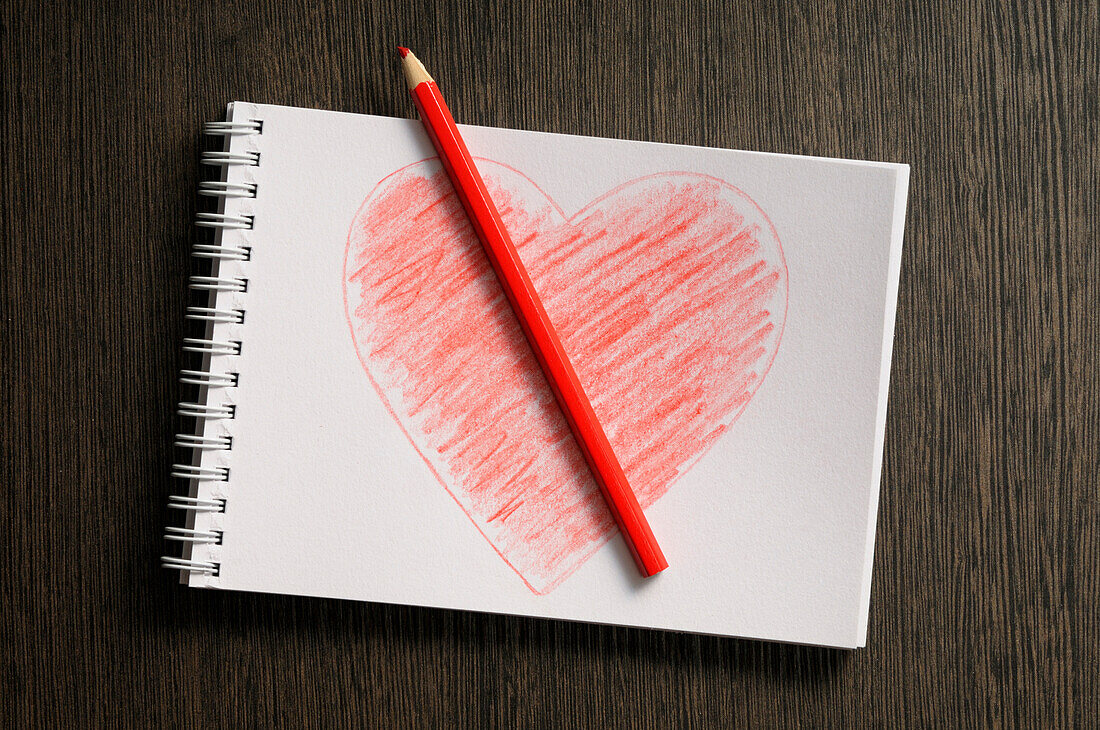 Herzförmige Zeichnung auf Notizbuch und Farbstift, Holzhintergrund, Studioaufnahme