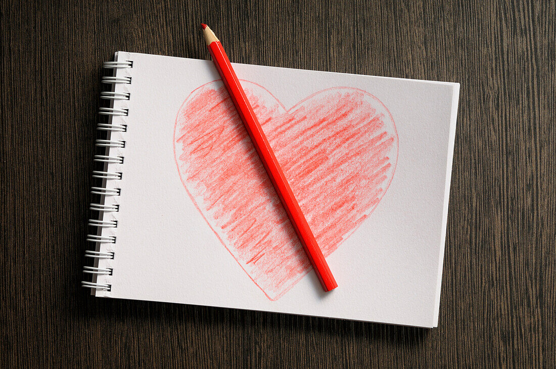 heart shaped drawing on notebook and colored pencil,wooden background,studio shot