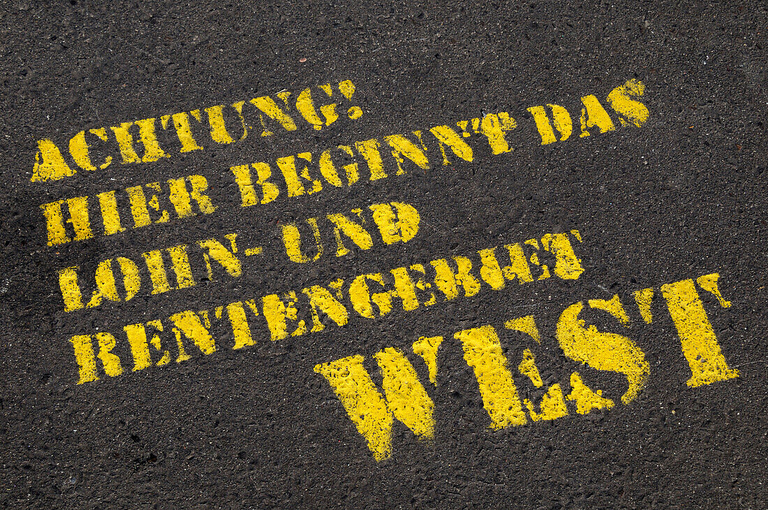 Nahaufnahme von deutschem Text auf gepflasterter Straße (Achtung, hier beginnt das Gebiet von Lohn und Rente West),Berlin,Deutschland