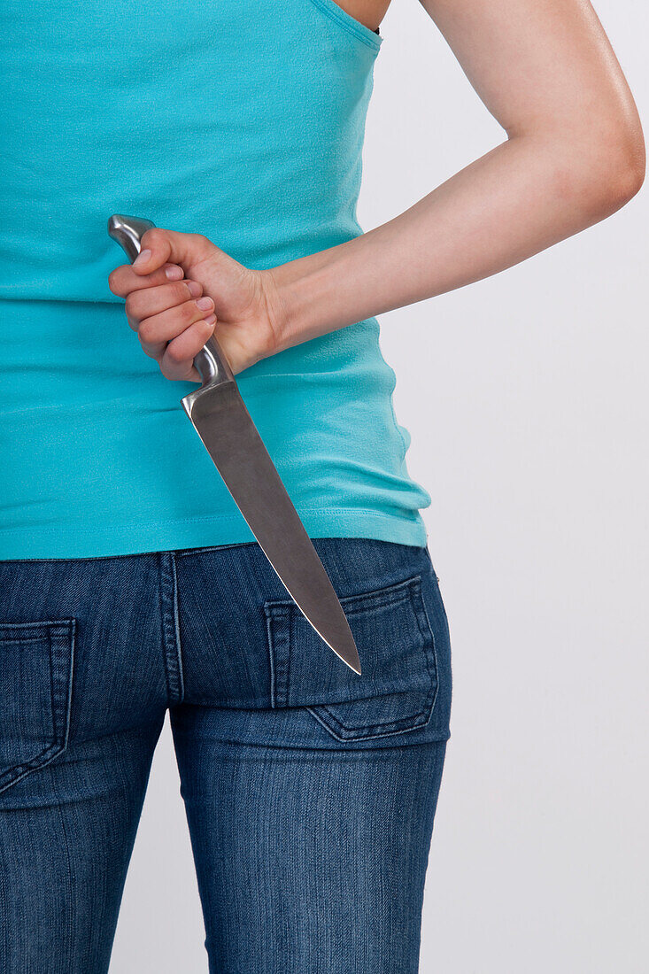 Frau hält ein Messer hinter ihrem Rücken