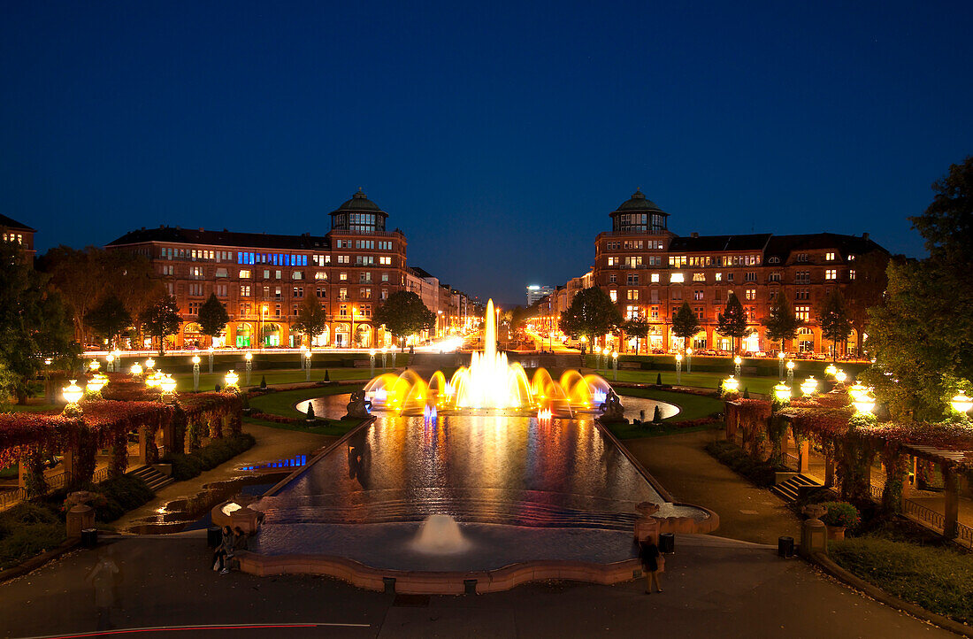 Blick auf einen nächtlichen Springbrunnen mit Arkadengebäuden im Hintergrund am Freidrichsplatz, Mannheim, Deutschland