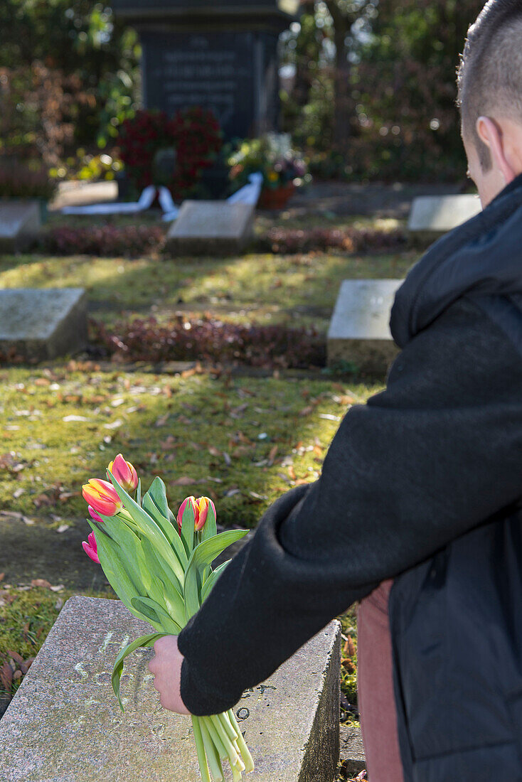 Rückansicht eines Teenagers, der eine Blume auf einen Grabstein auf dem Friedhof legt,Deutschland
