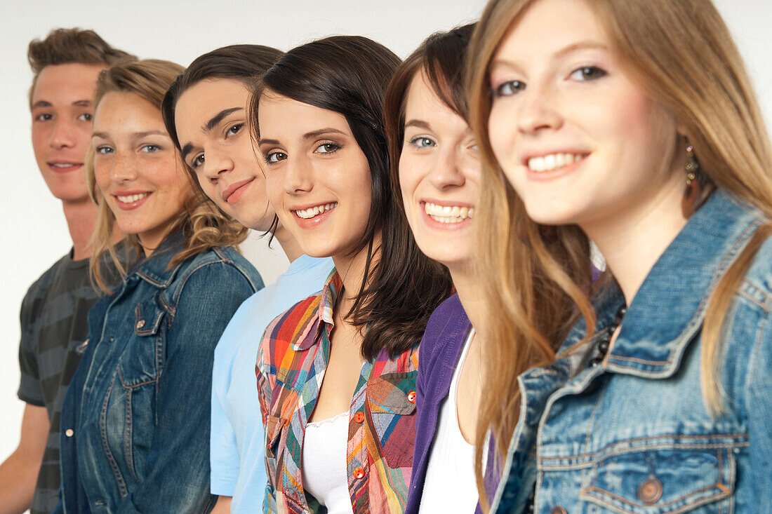 Close-up portrait of six,young men and young women in a row,smiling and looking at camera,studio shot on white background